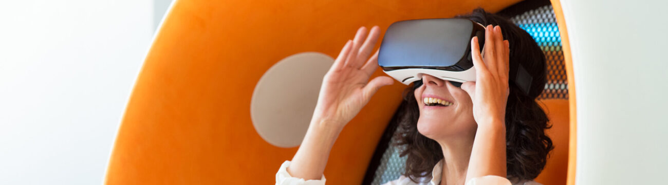 Happy businesswoman watching virtual presentation Happy businesswoman watching virtual presentation in studio. Woman wearing VR glasses, sitting in interactive chair, adjusting device and smiling. VR technology concept